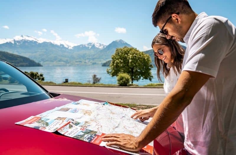 Couple looking at map of Switzerland on the bonnet of their car